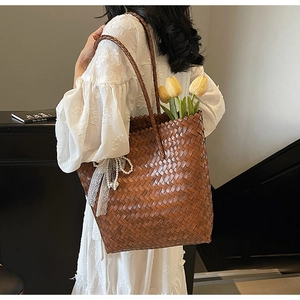 Détail d'un sac cabas en paille tressée marron avec charm en dentelle et tulipes