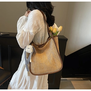 Détail du sac cabas en paille tissé avec sangle en cuir marron et pompon décoratif
