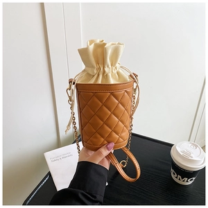 Detail view of brown quilted bucket bag with beige canvas drawstring and metal chain strap