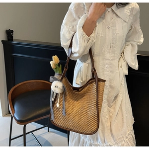 Détail d'un sac cabas en paille avec anses en cuir marron et pompon décoratif blanc