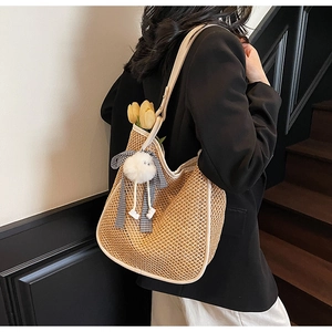 Détail du sac cabas en paille tissée avec bordure en cuir blanc et breloque à l'épaule