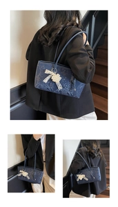 Detail of dark blue snake-embossed bag with lace bow and pearl charm on stairs