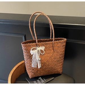 Détail d'un sac cabas en paille tissée avec nœud en dentelle blanche et breloque en perles