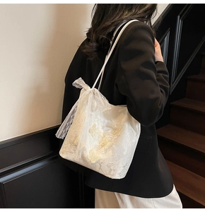 Dettaglio della borsa tote in pizzo avorio con ricami a farfalla 3D e fiocco decorativo