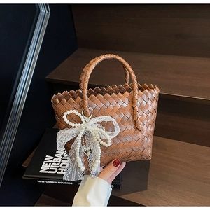 Détail du sac panier tressé marron avec nœud en dentelle et breloque cœur en perles
