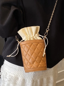 Brown leather and beige canvas quilted bucket bag with gold chain strap on model