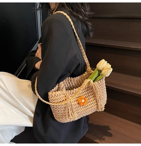 Detailed texture of hand-woven straw shoulder bag featuring an orange crochet flower detail