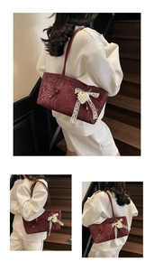 Detail of burgundy snakeskin embossed tote bag with a white pearl bow pendant