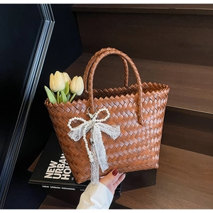 Détail d'un sac panier tressé marron avec nœud en perles et charme en dentelle sur bois