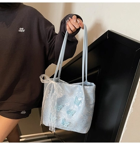 Dettaglio del ricamo a farfalla 3D e fiocco in pizzo bianco su borsa tote celeste