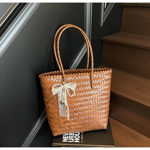 Détail du sac cabas en paille marron avec nœud en dentelle blanche et pendentif