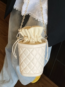 Quilted cream drawstring bucket bag with gold chain strap for an elegant retro look