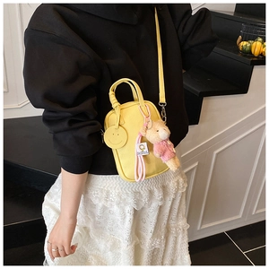 Detailed view of yellow mini crossbody bag with a smiling face tag and plush bear charm