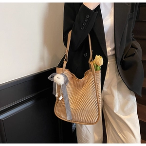 Détail du sac cabas en paille tressée avec un nœud à carreaux et un accessoire peluche