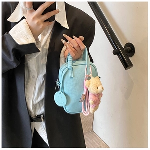Detail of light blue mini bag featuring lychee texture and cute bear charm accessory