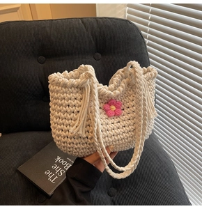 Close-up of cream woven bucket bag with pink crochet flower and thick shoulder strap