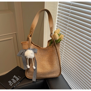 Détail d'un sac cabas en paille tissée avec anses en cuir brun et décoration florale