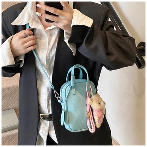 Close-up of light blue pebble leather crossbody bag with cute teddy bear charm detail