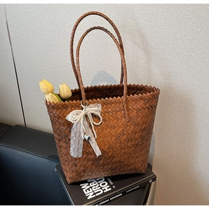 Détail du sac panier tressé avec nœud en dentelle blanche et pendentif perle élégant