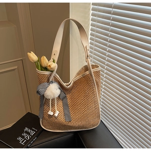 Détail du sac cabas en paille tressée avec anses en cuir blanc et pompon peluche