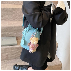 Detail of light blue textured leather crossbody bag with a plush bear charm and smile tag