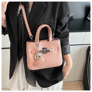 Pink lychee grain leather bucket bag with silver lock and heart charm on a black blazer