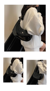 Detailed macro view of black patent leather hobo bag with gold logo and shoulder strap