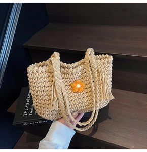 Detail of hand-woven beige tote bag featuring a bright orange crochet flower and tassels