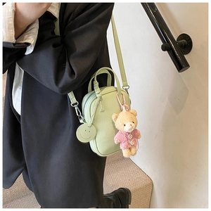 Detail of light green faux leather crossbody bag with teddy bear and smiley charm