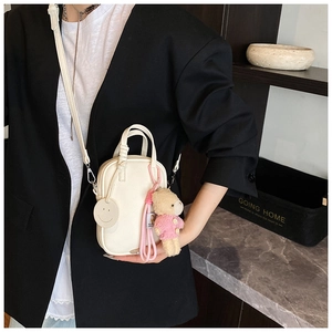 Detail of cream mini crossbody bag with litchi leather texture and a cute bear charm