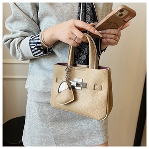 Detail of beige lychee pattern bucket bag with silver twist lock and heart pendant