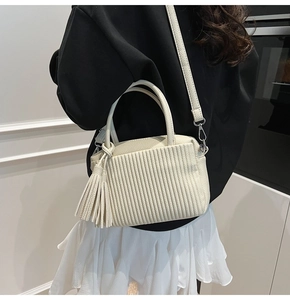 Détail du sac bandoulière blanc cassé avec texture plissée et breloque à long pompon