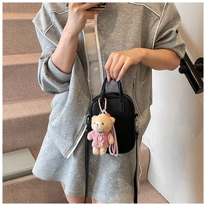 Detail of black pebbled leather crossbody bag with cute pink teddy bear plush charm