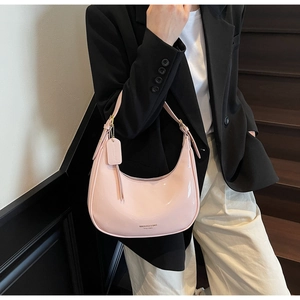 Detail of pink patent leather hobo bag worn on shoulder showing texture and gold logo
