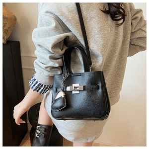 Detail of black litchi texture handbag with silver twist lock and small charm