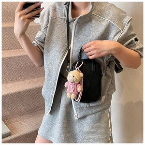 Close-up of mini black litchi leather crossbody bag with a cute pink bear plush charm