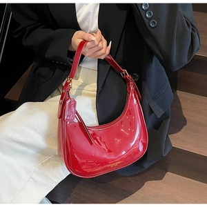 Detail of red patent leather crescent underarm bag with gold logo and metallic hardware