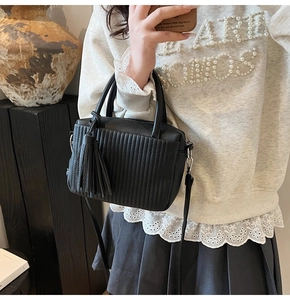 Détail du sac à main noir montrant la texture plissée verticale et le gland en cuir