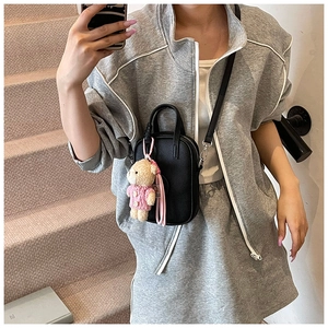 Detail of black litchi grain leather crossbody bag with a cute plush bear pendant