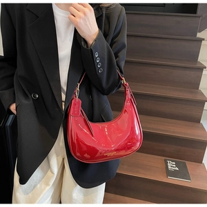 Detail of red patent leather crescent bag with golden MIKAQI logo on a black suit backdrop
