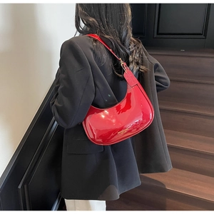 Side view of red patent leather hobo bag with gold logo on a black blazer