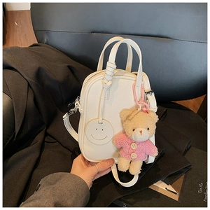 Close-up of white litchi pattern mini bag featuring a plush bear and smiley face charm