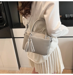 Détail d'un sac à main gris clair plissé avec breloques à pompons longs et poignée chic