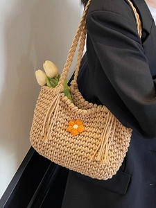 Chic beige woven tote bag with orange floral detail and fringe on a model wearing black