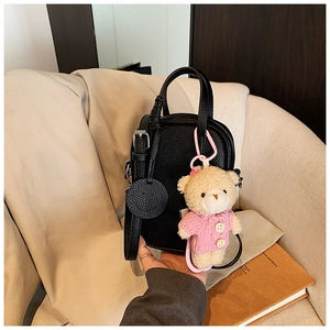Detail of black litchi grain leather handbag with plush bear charm on beige sofa