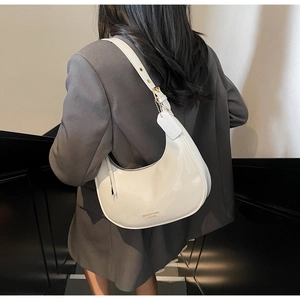 Detail view of a white patent leather saddle bag worn by a model in a modern setting