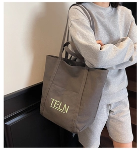 Detail of grey canvas tote bag with vibrant green TELN lettering and front pocket