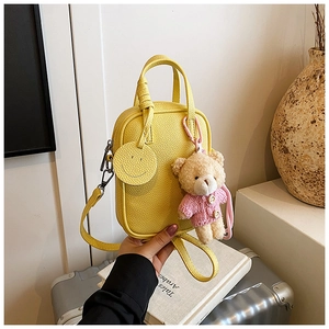 Detail of yellow lychee leather mini crossbody bag with cute teddy bear and smiley charm