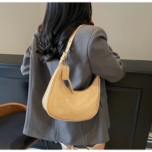 Close-up of beige patent leather half-moon bag with adjustable strap and gold hardware