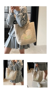 Detail of canvas tote bag showing beige texture, green embroidery, and outer pocket
